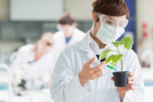 Woman standing at the laboratory while holding a plant adding chemical to soil with syringe.jpeg